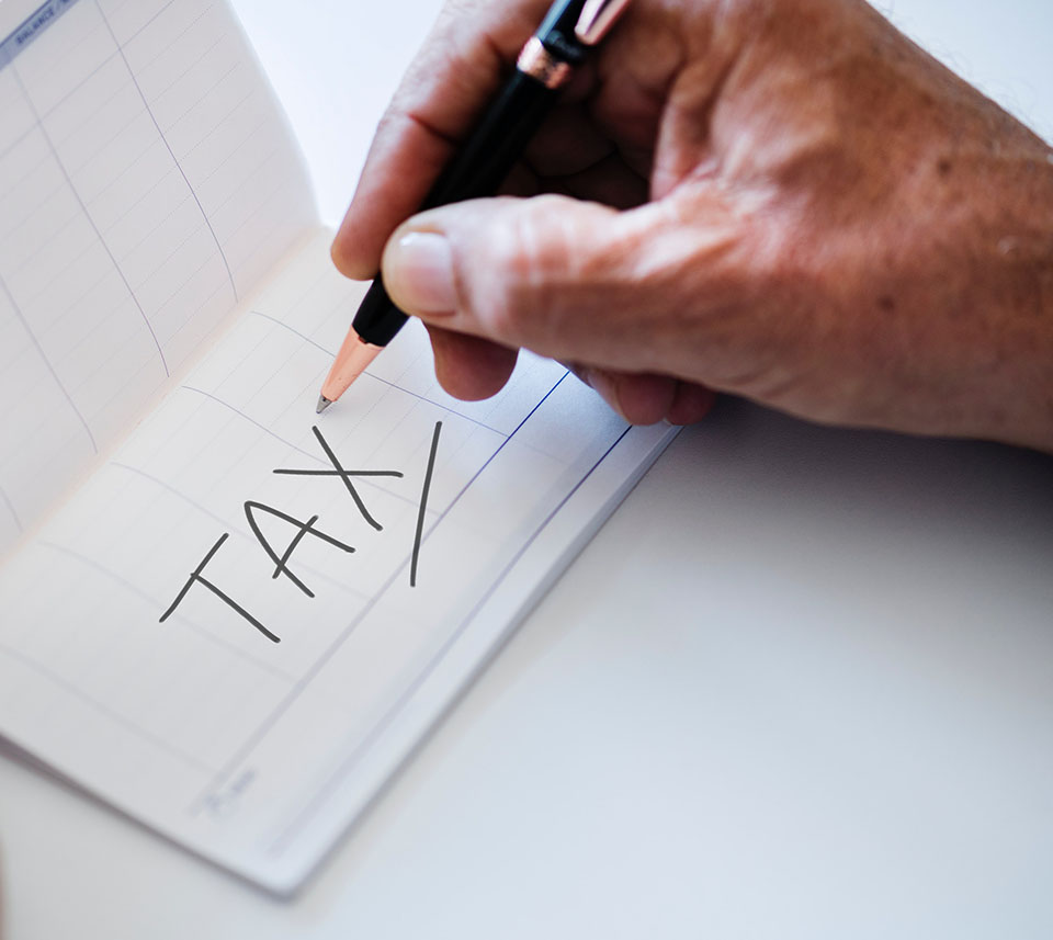 person holding pencil over a piece of paper with the word tax written on it