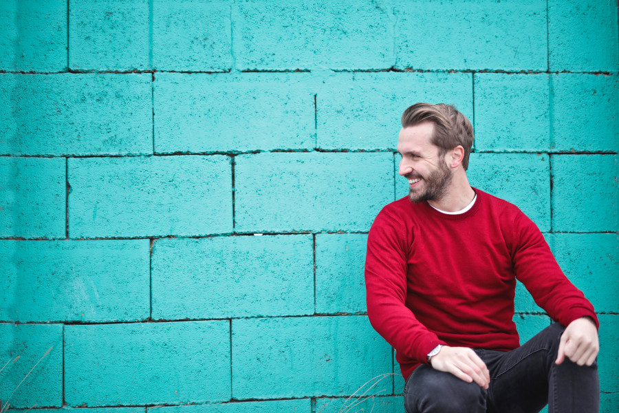 picture of bearded man smiling against a blue brick wall in a happy mood. Understand the mood of your customer when defining your audience