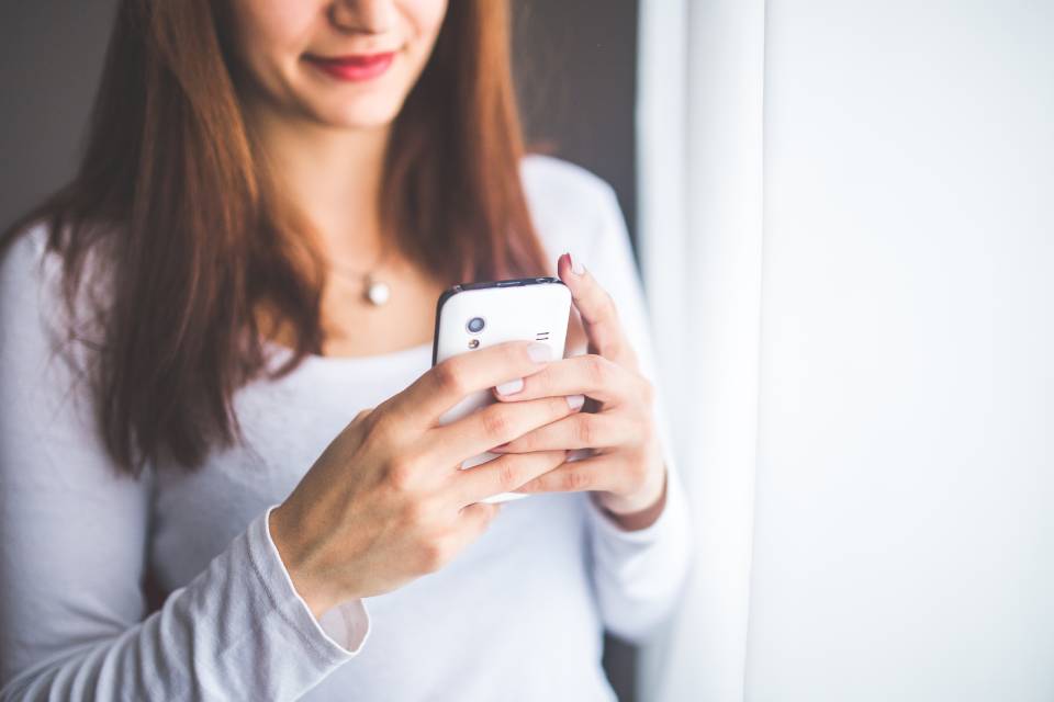 Woman holding a mobile phone. With a mobile invoicing app, she can create and send invoices from anywhere.