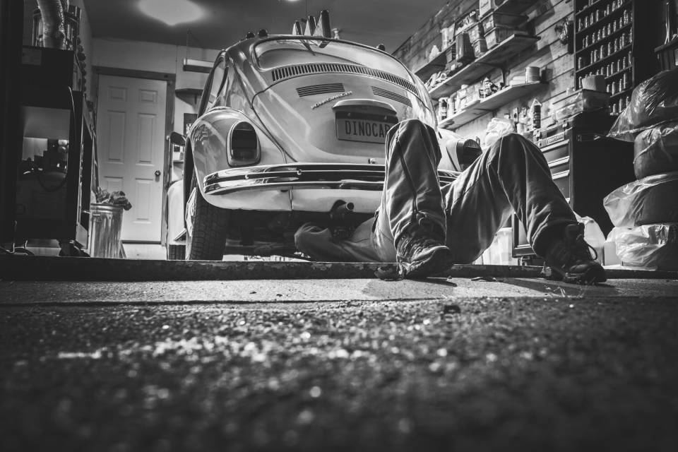 A black & white photo of a man working on an old VW Beetle in a garage