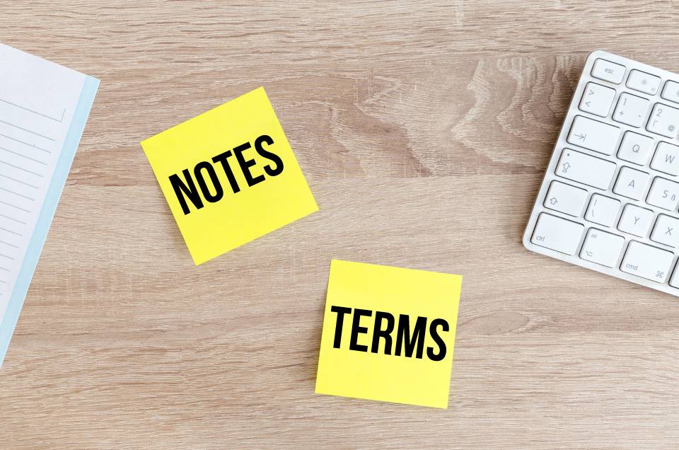 Two yellow post-it notes next to a computer keyboard that say 'Notes' and 'Terms'