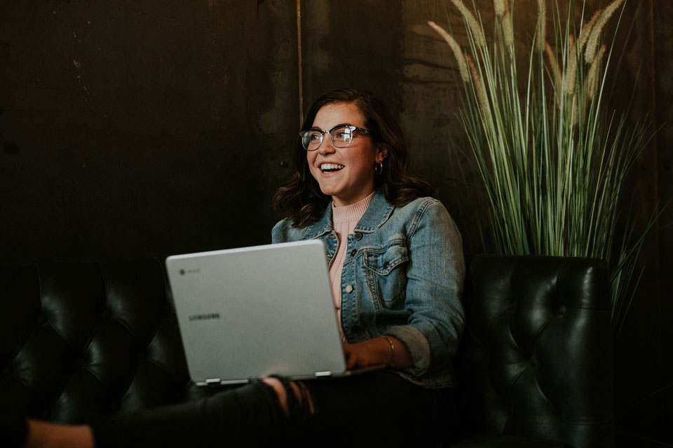 Girl on a computer on a sofa looking happy. Probably about her online, cloud-based bookkeeping solution.