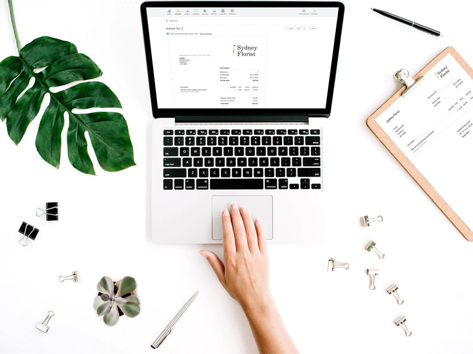 A desk with a printed invoice and a laptop using Debitoor invoicing software to create an Australian tax invoice