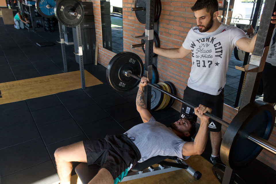 Trainer spotting a client doing a bench press in the gym.