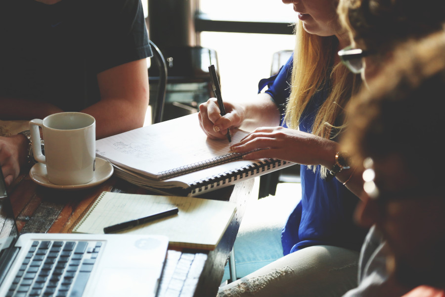 image of people around a desk in coffee shop with laptops and notepads, like they are having an impromptu meeting or lecture