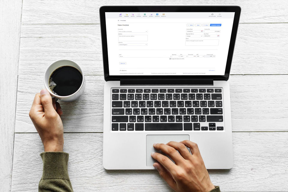 Invoicing software like Debitoor, shown on the laptop this man drinking coffee is working on, makes it easy to create & send professional invoices.