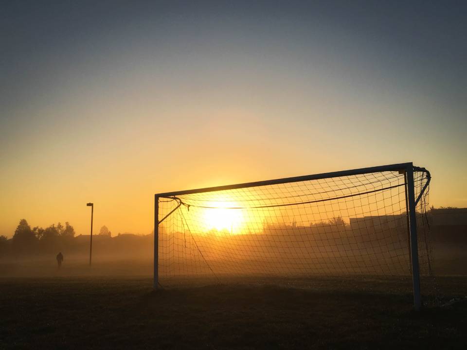 Image of a football goal with the sunrise in the background. Keep your main business goals in mind when prioritising