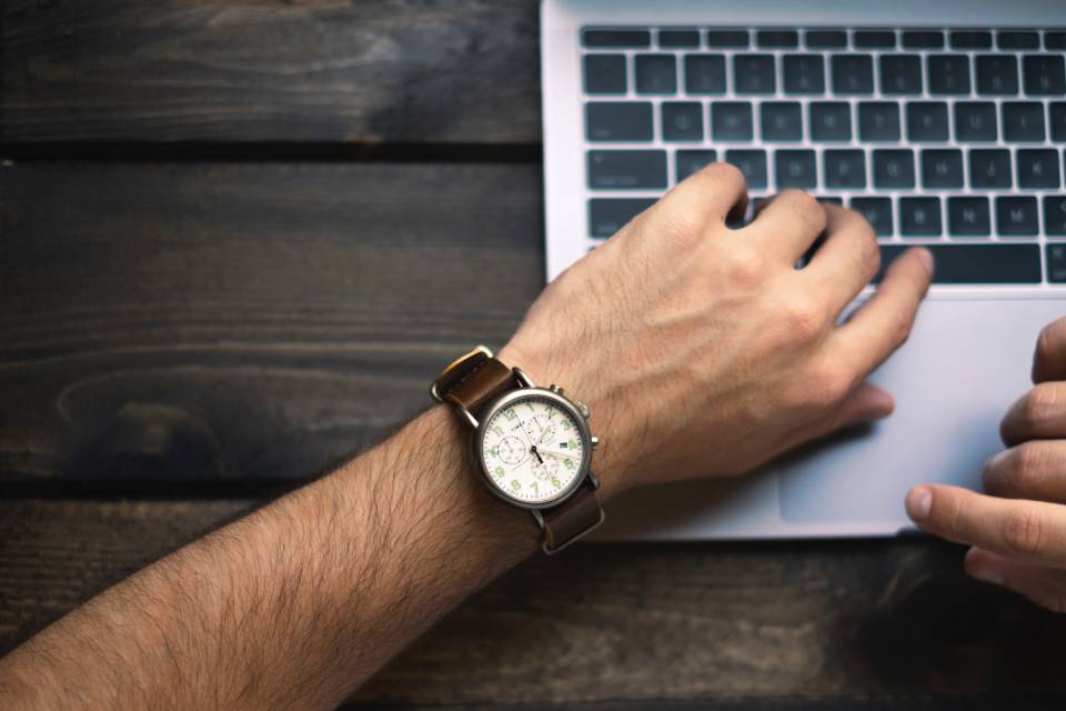A man looking at his watch over a laptop. Manage your own working hours as a freelancer.